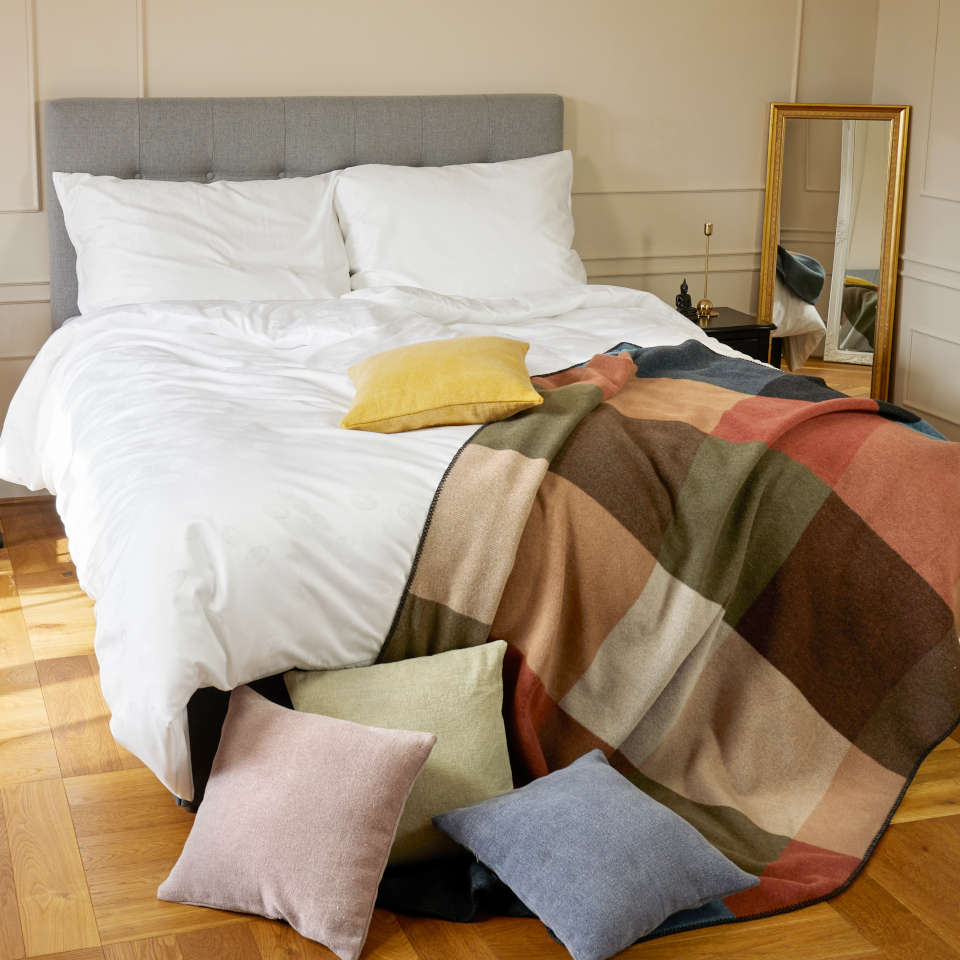 Postel v bytě, kde jsou produkty SCANquilt - vlněný pléd a barevné povlaky na dekorační polštářky